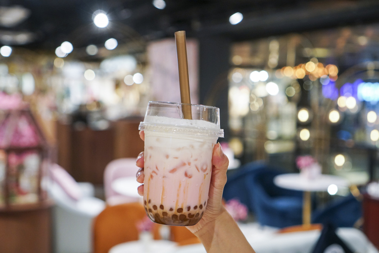 Woman holding a plastic cup of rose tea with golden bubble/boba, topped with milk foam, what does rose milk tea taste like? Sakura Milk Tea